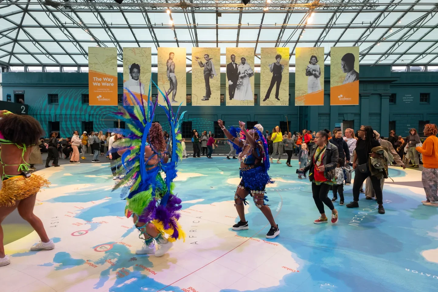 Photo showing people dressed in vibrant costumes dancing on a big map inside a large atrium