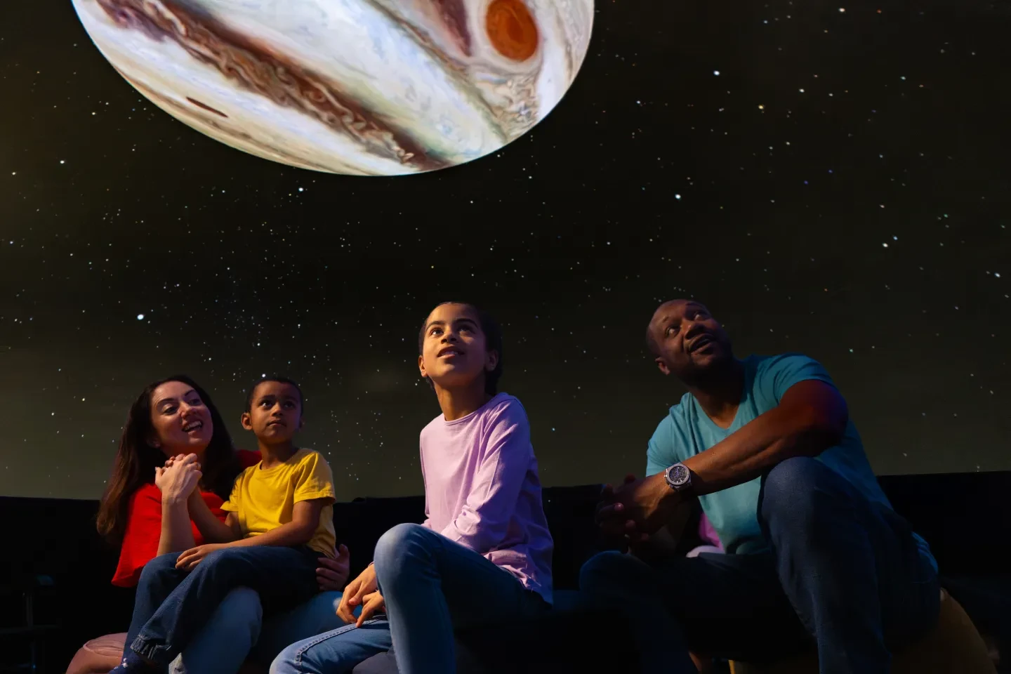 A family wearing colourful t-shirts and jeans look up at the planetarium show, part of Astronomers Take Over at the National Maritime Museum