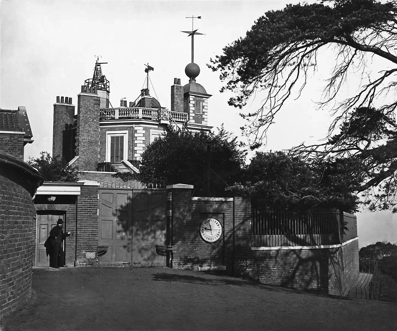 Nineteenth century photograph of the entrance to the Royal Observatory. The gates are closed and a policeman stands watch outside.
