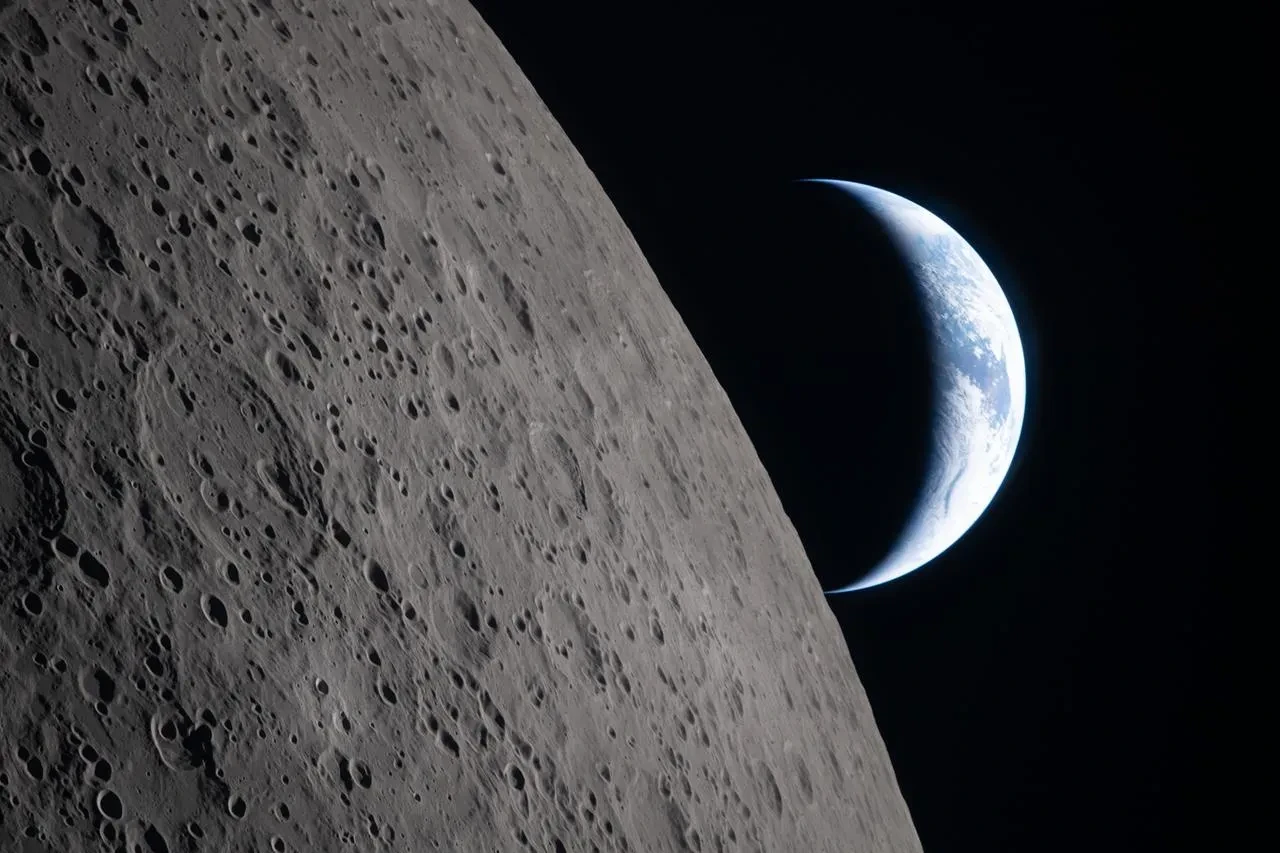 A section of the Moon in the foreground with Earth half in darkness behind to the right