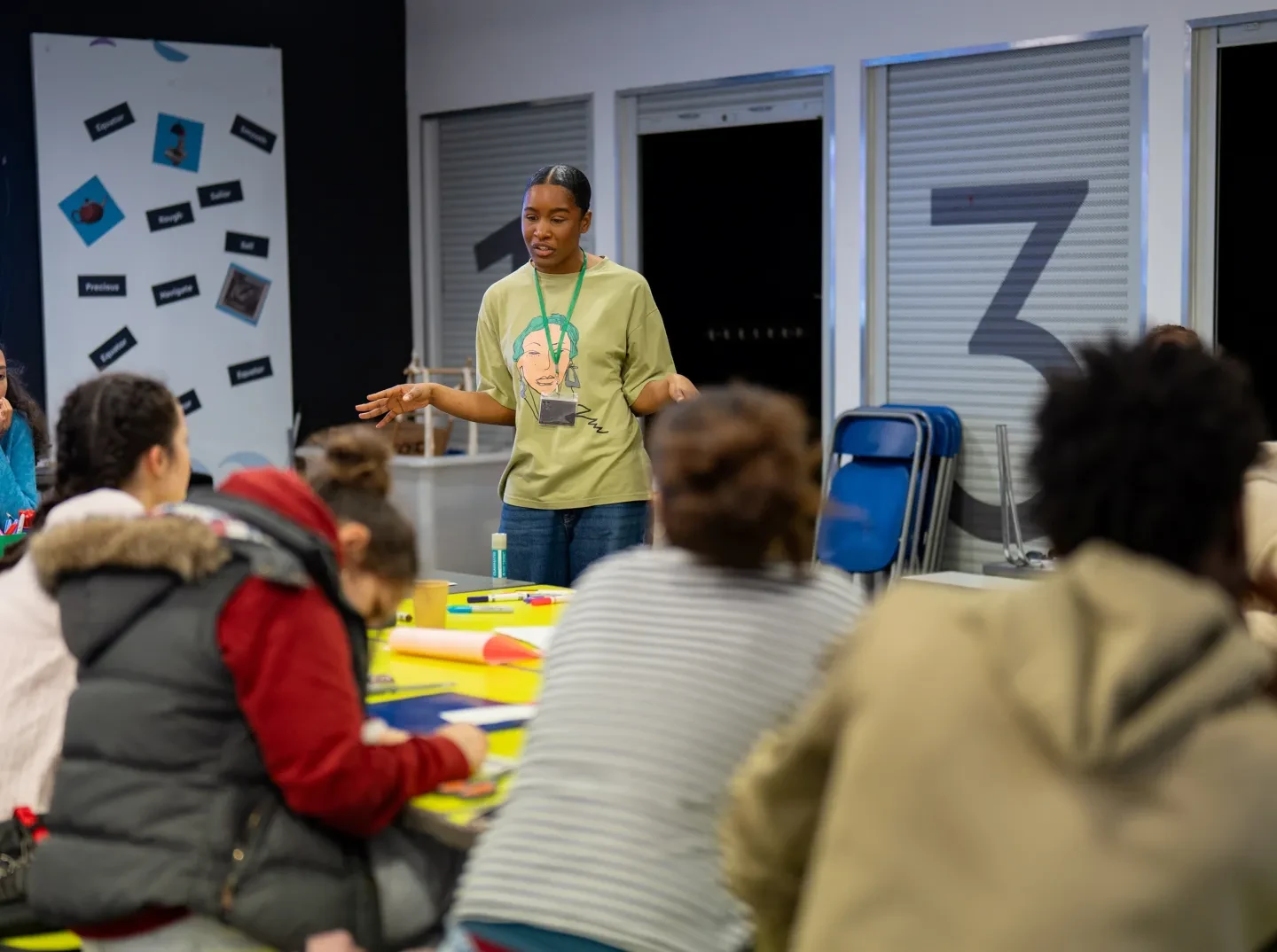 A woman called Chioma stands at the front of a group of young people listening to her explain an art activity
