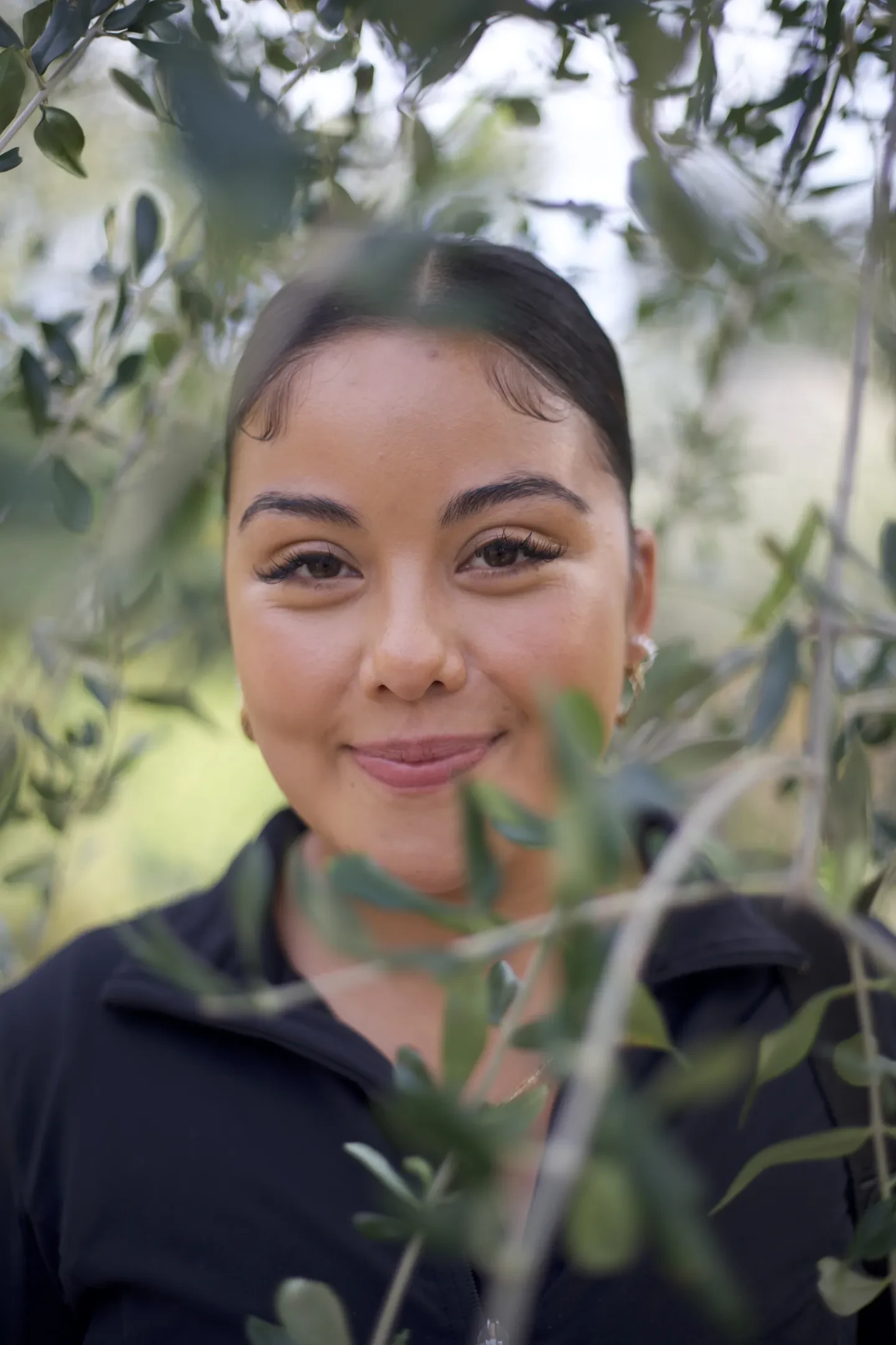 A headshot of Lirayen, looking through some branches. Lira is a London-based outdoor content creator, community builder, and nature enthusiast using her platform @OutsidewithLira to reframe what it means to belong in the outdoors.