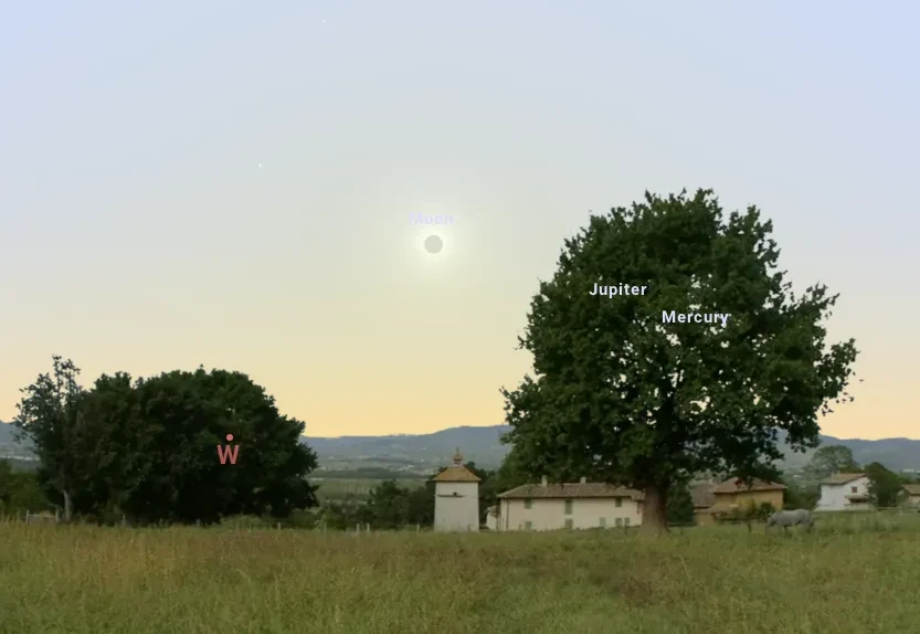View looking west showing Moon eclipsing the Sun low in the sky, with a landscape around and the event nearly going behind a tree
