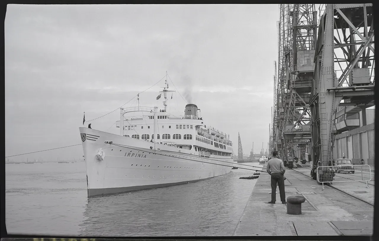 Black and white photograph of the passenger ship Irpinia, with a man standing on the side of the dock in the foreground