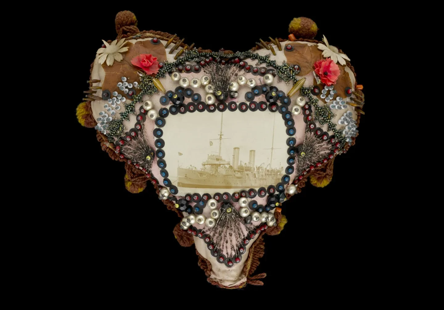 A heart-shaped cushion in embellished pink and white silk, with photograph of a ship in the centre.