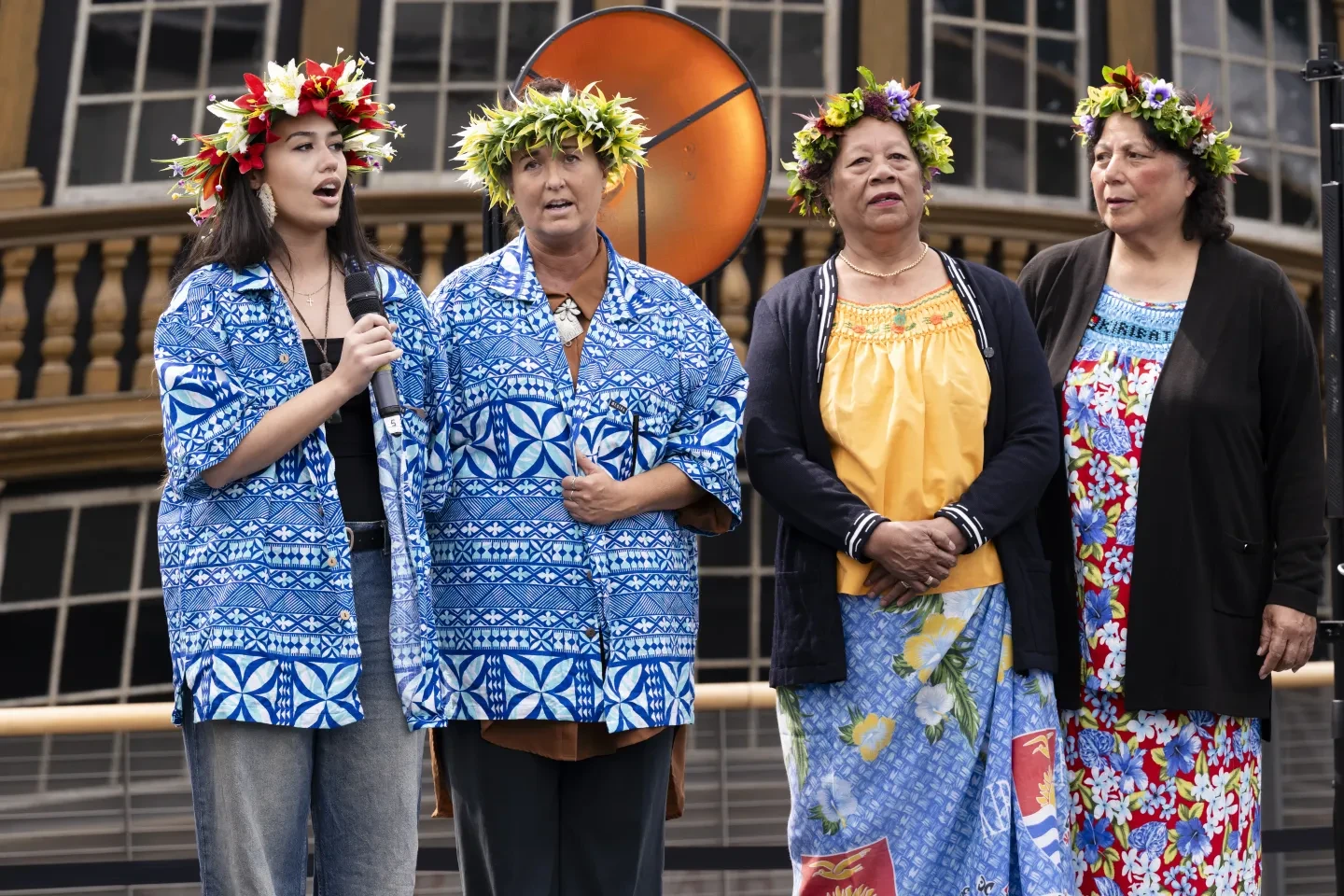 Photo of four women standing together wearing printed clothing and flower headdresses