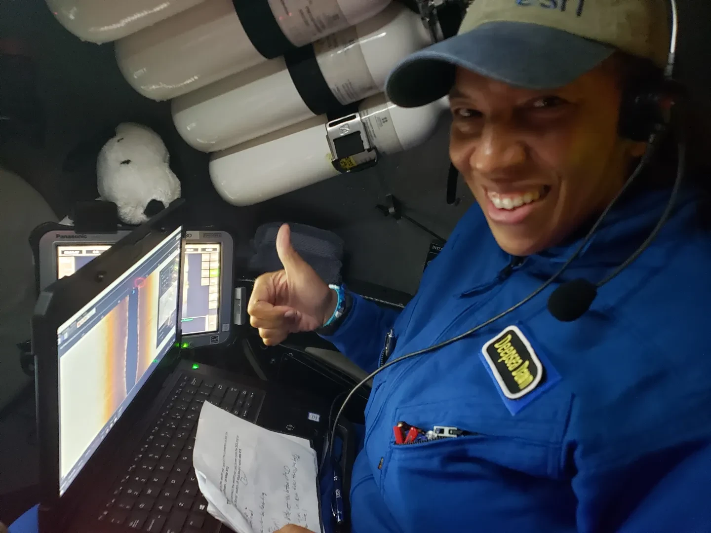 Oceanographer Dawn Wright gives a thumbs up while inside a submersible. Her toy Snoopy is visible to the left, placed above a display screen for the sub