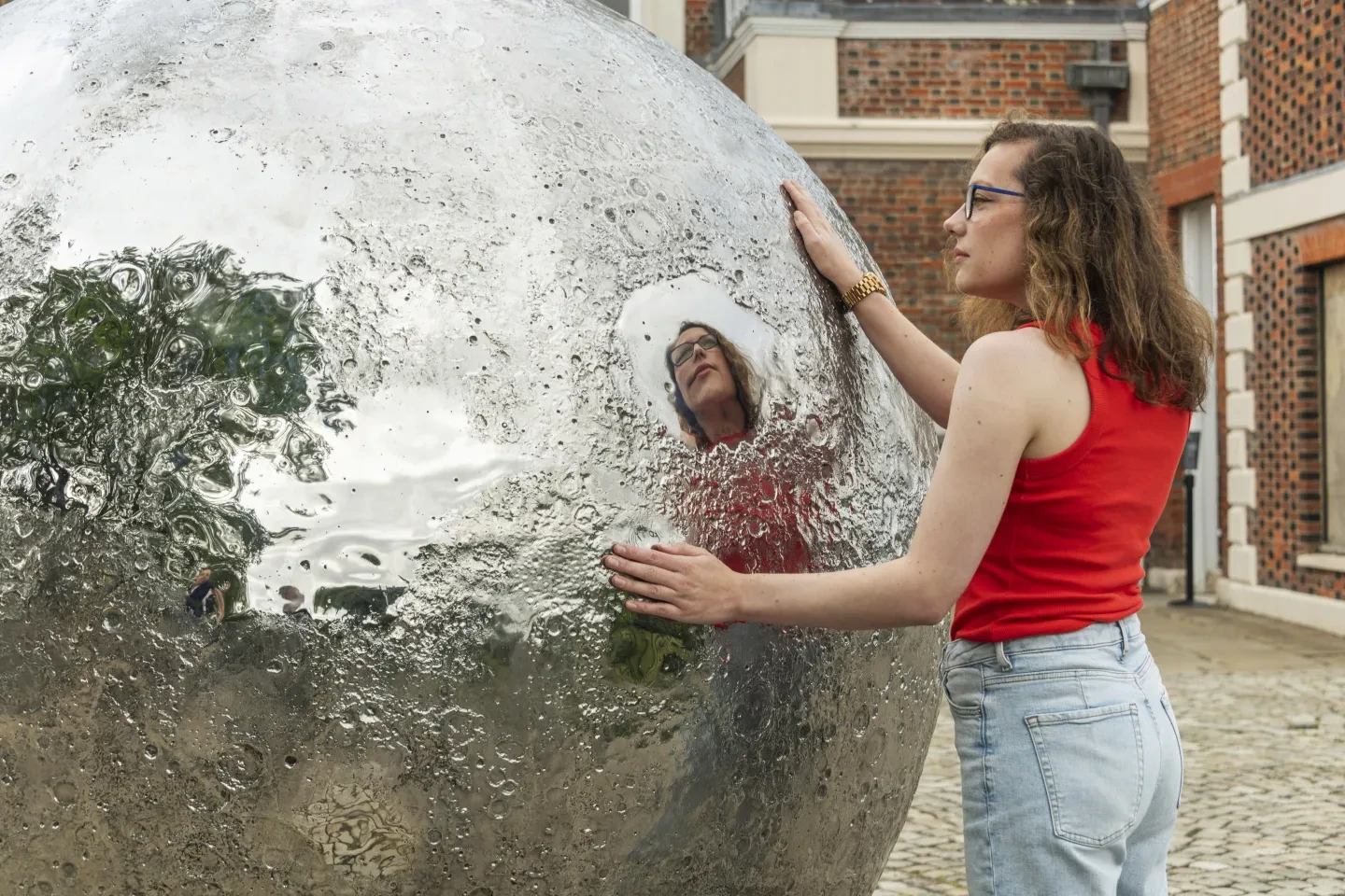 A woman in a red vest looks closely at the craters on the Mirror Moon sculpture at the Royal Observatory in Greenwich