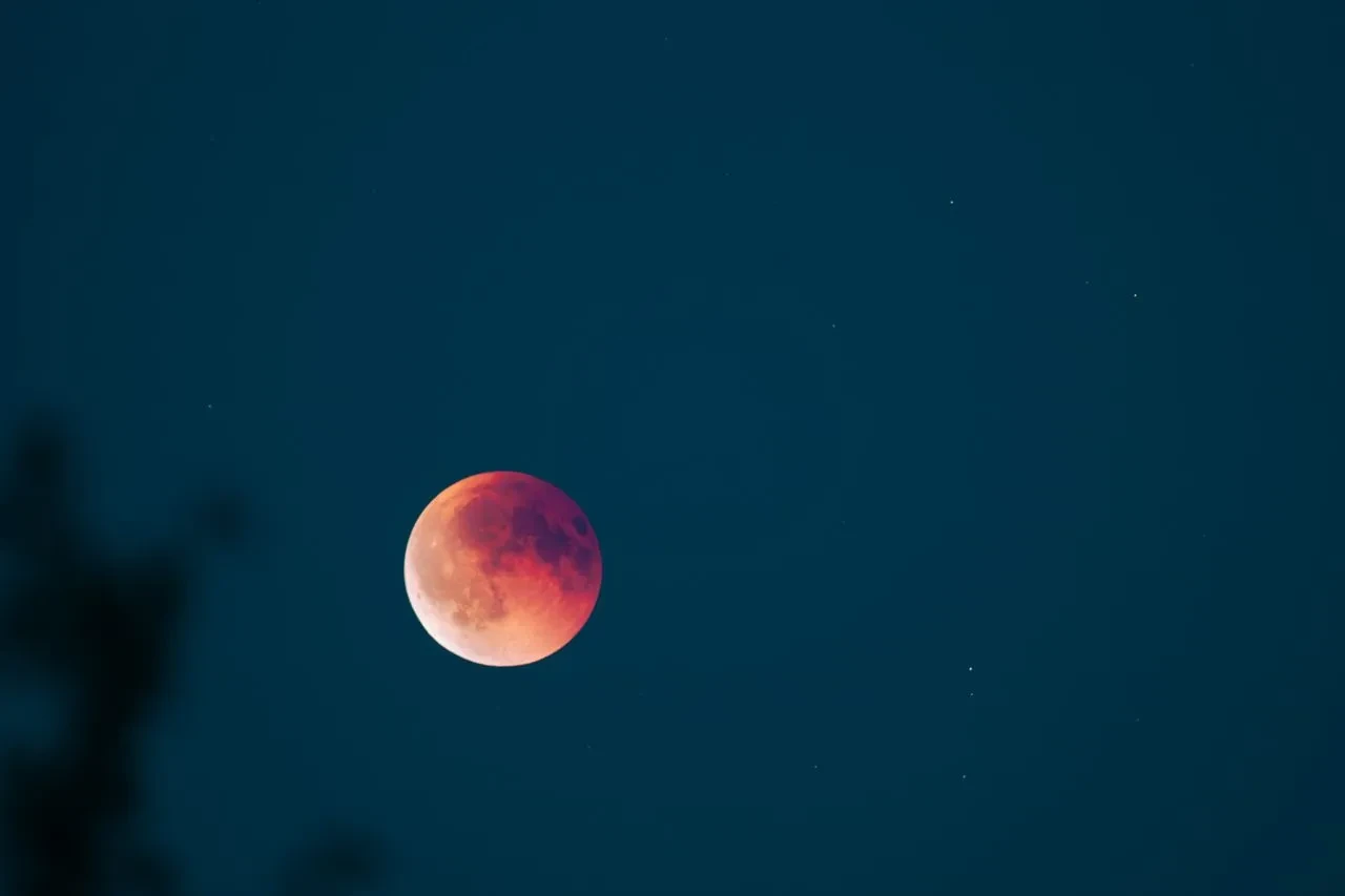 Moon photographed in partial eclipse, deep red on upper right limb fading to lighter red and usual silver