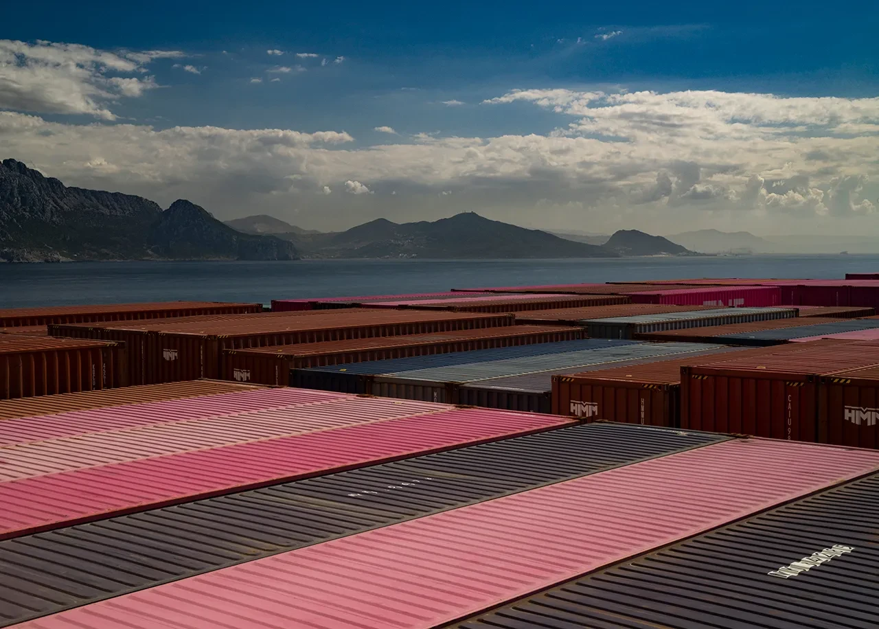 A ship at sea with containers stacked on board, and a view of mountains in the background