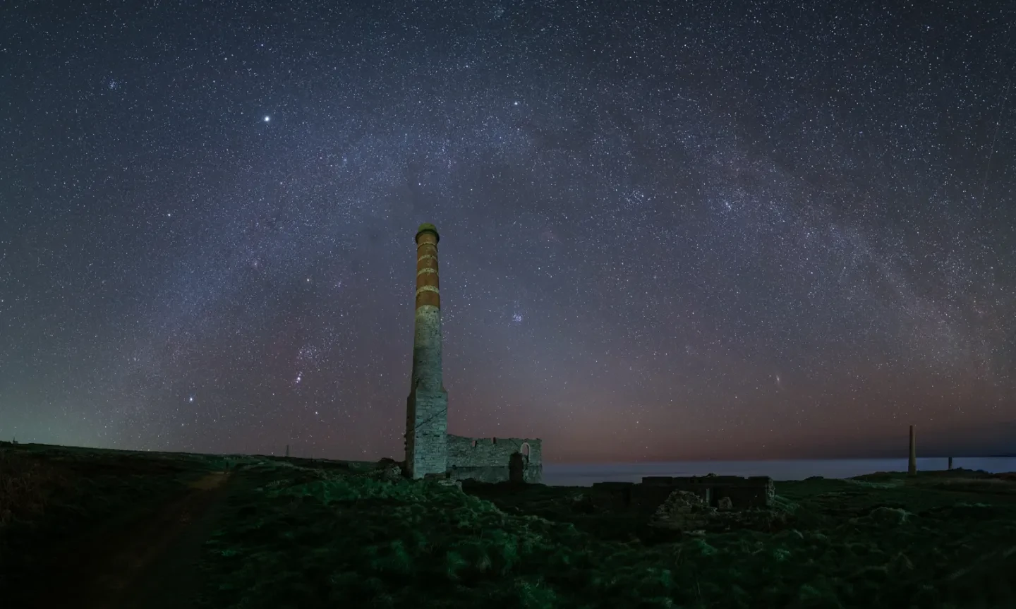 Milky Way arch over coastal landscape with ruined structure with tall chimney