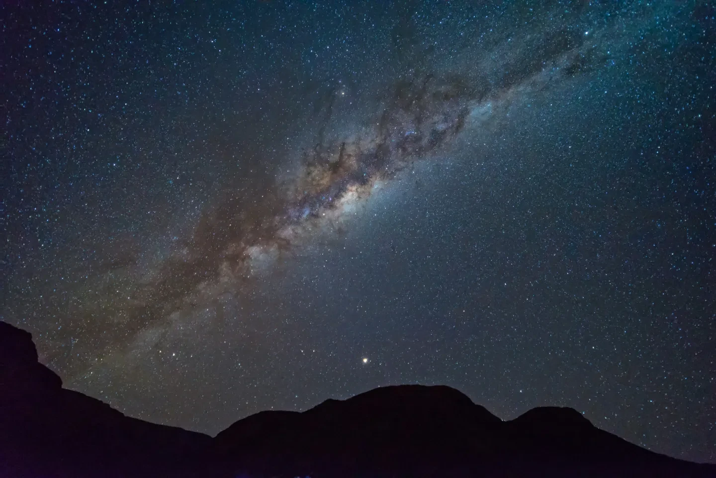 Milky Way in sky in dark and light patches over shadowy mountains
