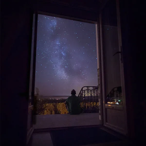 A person sitting in a doorway is silhouetted against a starry night sky.