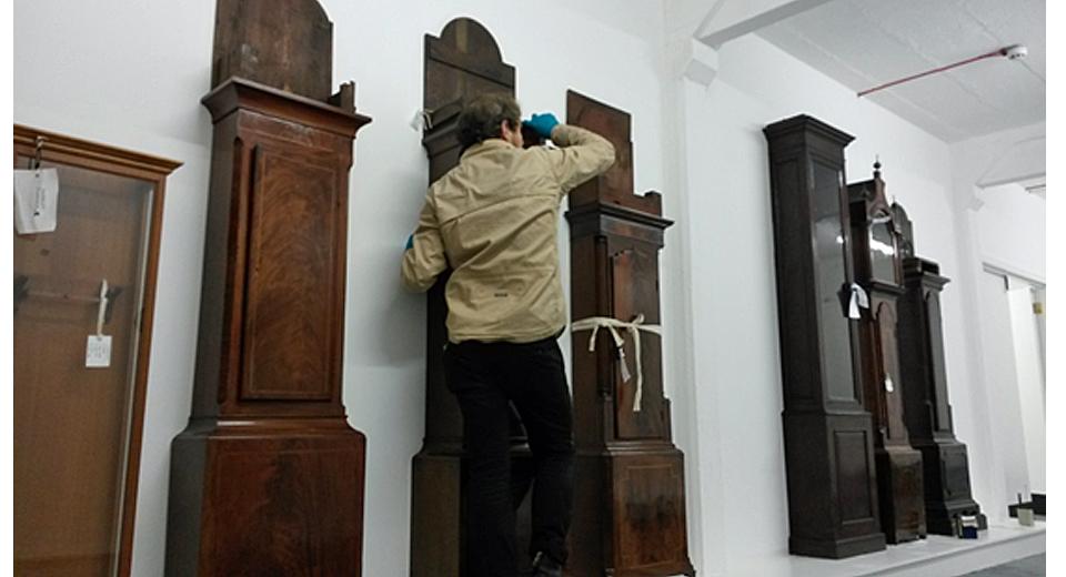 Art Object Handler fixing empty longcase clock trunks to plywood-clad walls in new store