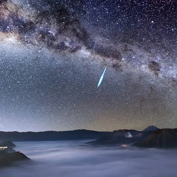 A meteor shower in a starry night sky above a cloudy mountain range.