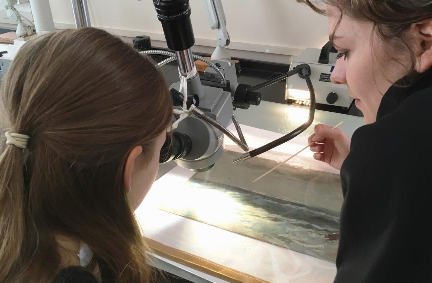 Katharine examining one of the Everett paintings under the microscope with Chloe Mills, Intern in Paper Conservation.