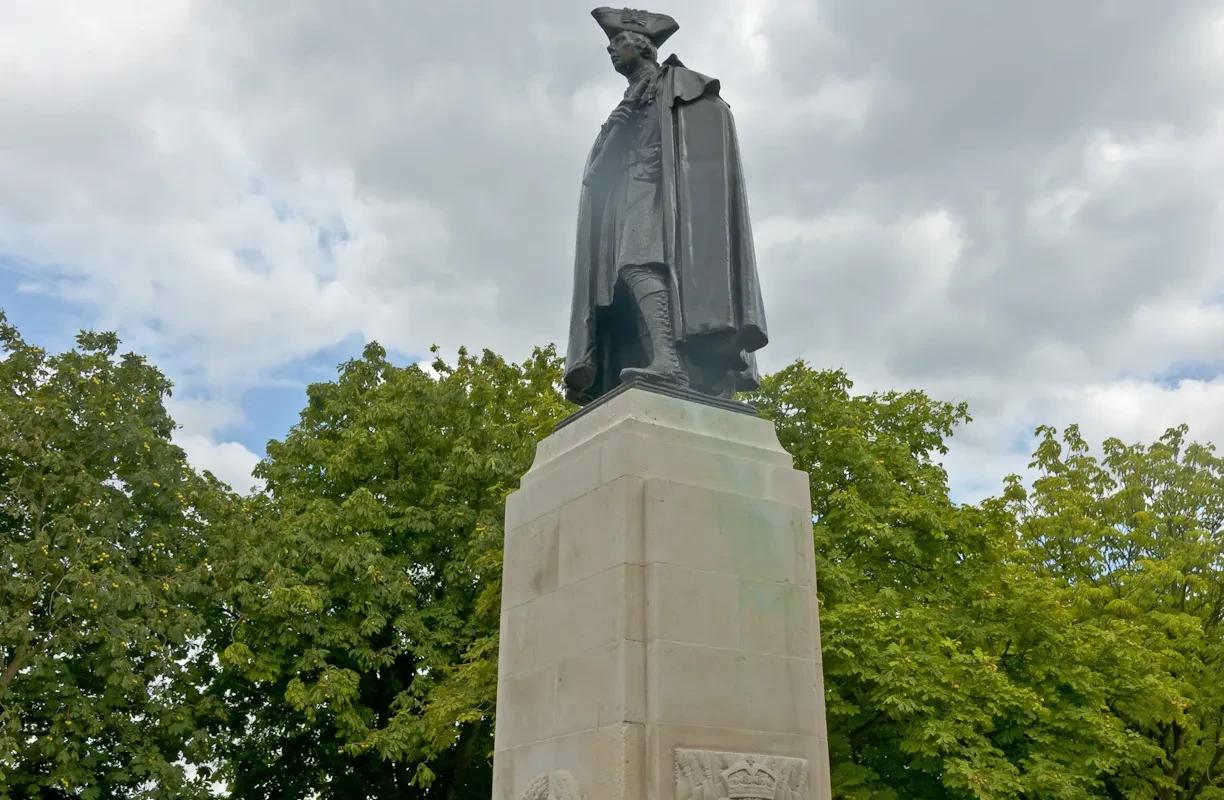 A statue of a man in a cape and tricorne hat on a stone plinth.