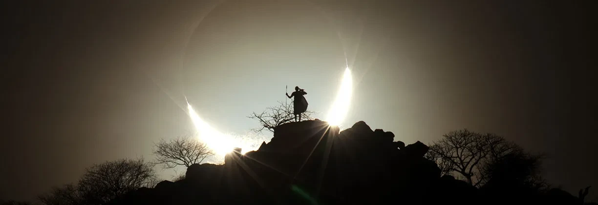 A person on a hilltop silhouetted by a solar eclipse. 