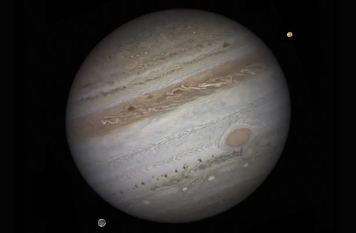 Jupiter with swirling clouds and two small, bright moons, Io and Ganymede.