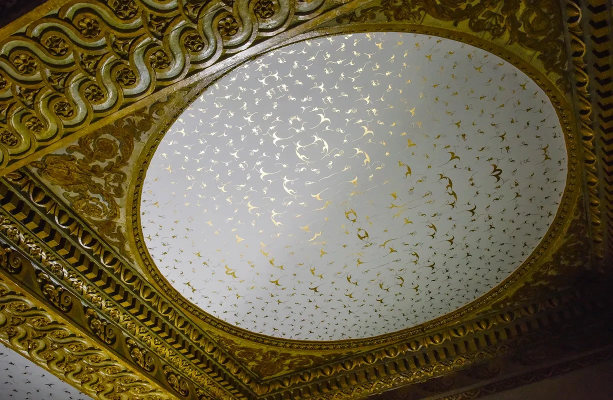A white and gold circular ceiling feature is framed with ornate gilded moldings.
