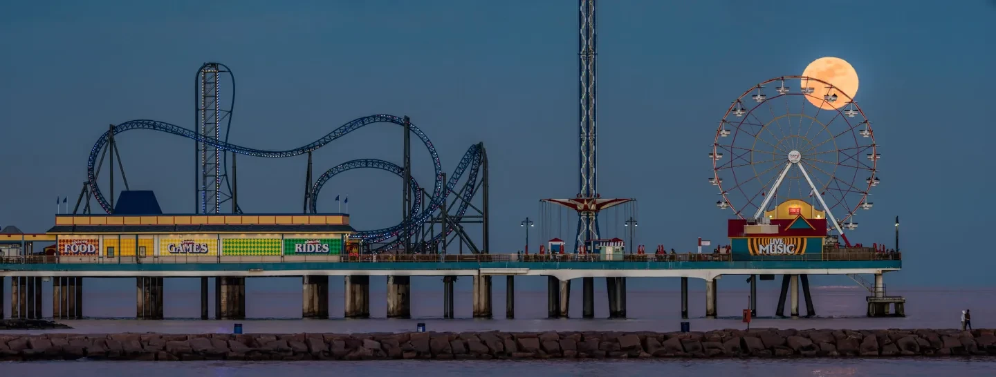 Night photograph of the moon rising above a pier fairground.