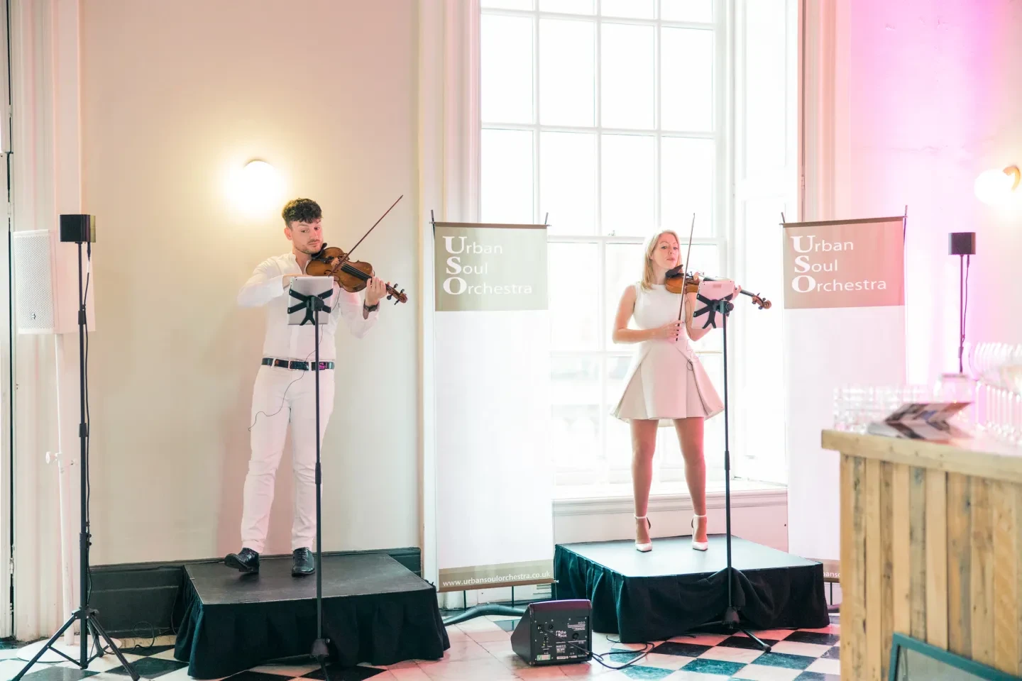 Two violinists in white on stage, with signs saying Urban Soul Orchestra.