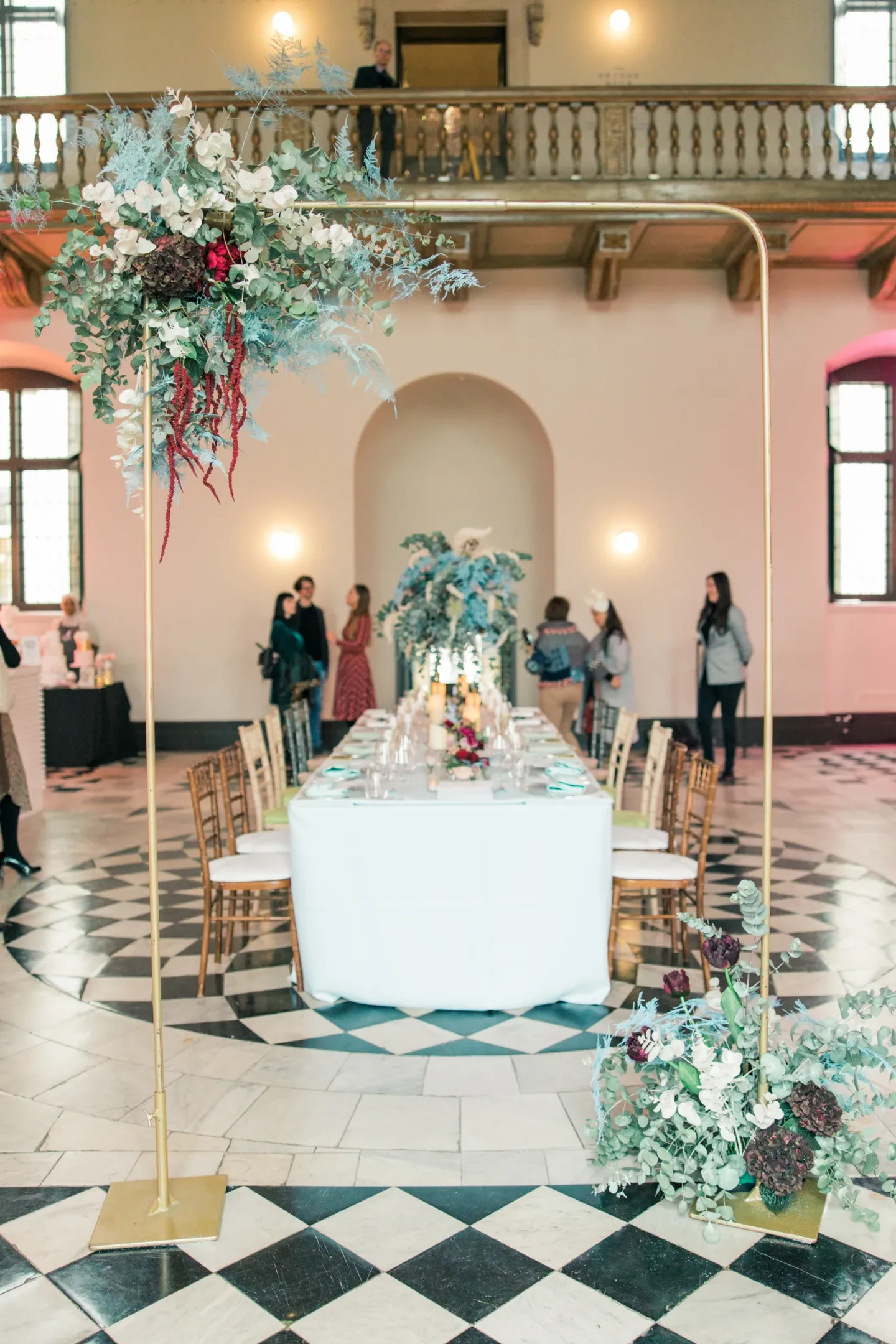 Floral arrangements and a set table on a black and white tiled floor.