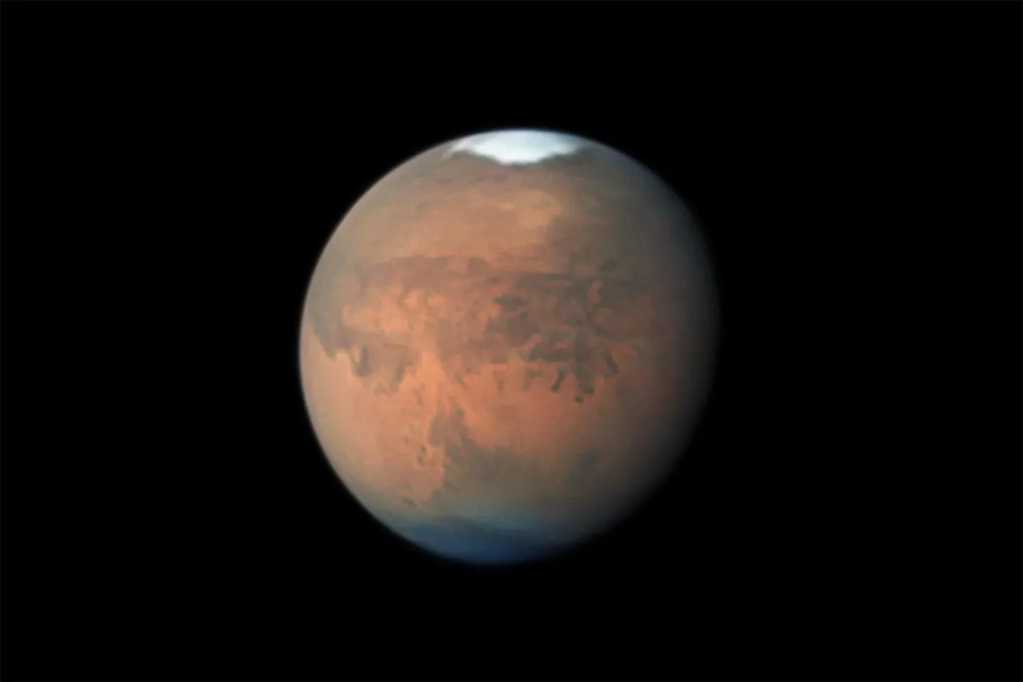 Astronomy photograph of the red planet, Mars, with a white area at its top. 