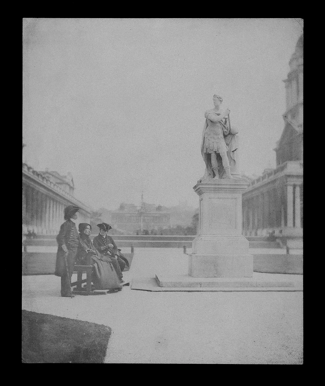 A negative image showing two naval captains and an elderly lady outside, next to a classical statue.