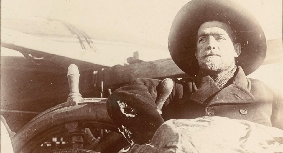 Historic photograph of explorer Sir Ernest Shackleton standing by the wheel of the ship Discovery