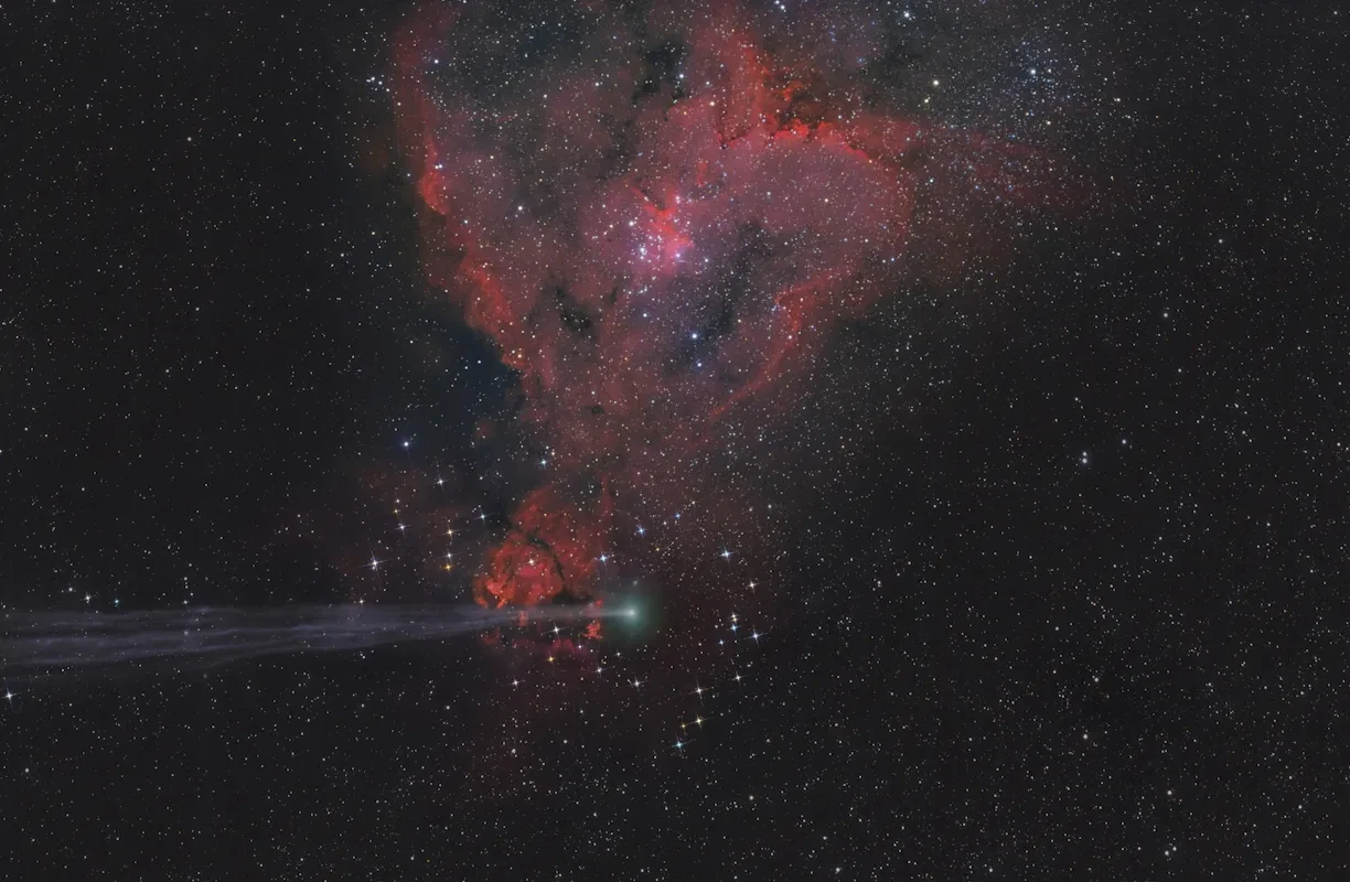 A comet passes a colourful nebula in a starry sky.