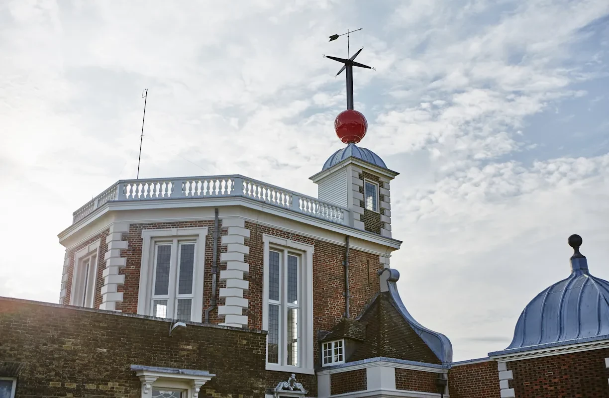 A red ball at the foot of a weathervane on the Flamsteed house roof.