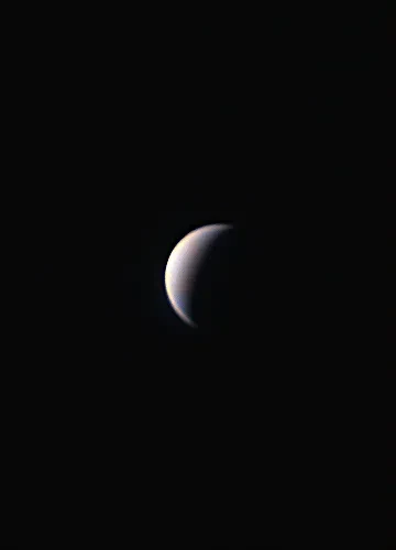 A white crescent planet in a black sky.