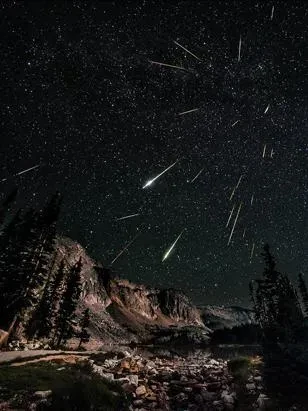 A meteor shower in the black night sky above a mountain range.