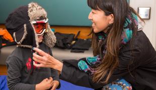 A child tries on a black puffer jacket and goggles