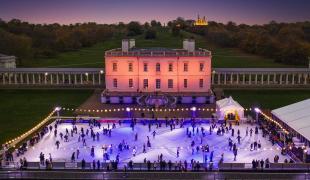 Image of the Queen's House in Greenwich lit in pink lights at dusk, with ice rink in front with lots of people on it, lit up in blue