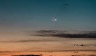 Image of new crescent Moon against the sky with sunset and black clouds