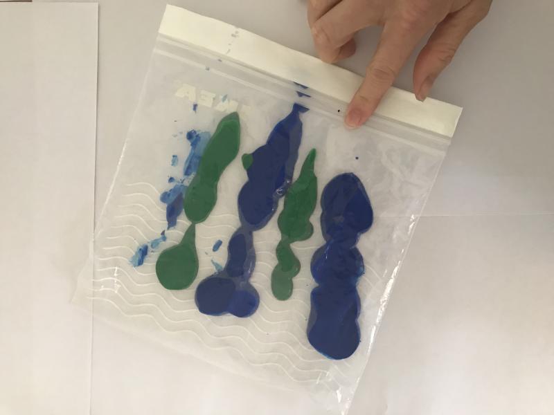 Plastic sandwich bag with top taped shut and lines of blue and green paint