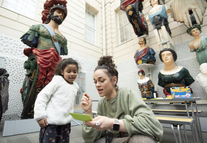 An adult and child are looking at a piece of paper. In the background are figureheads.