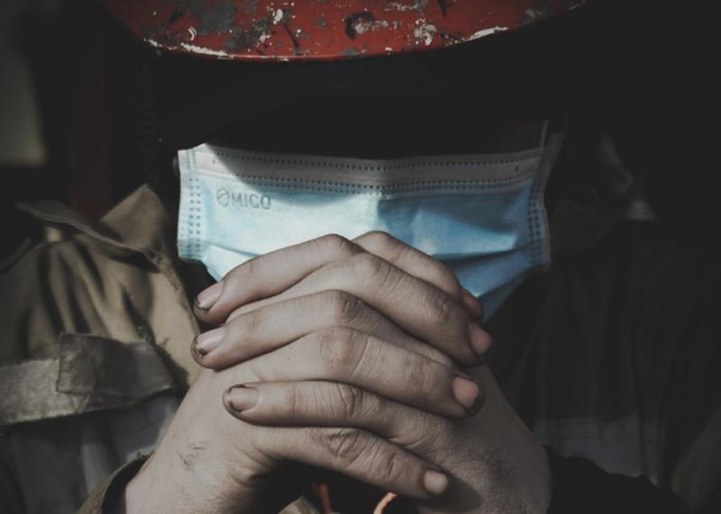 A seafarer clasps his hands in prayer. His face is in shadow, but he is wearing a mask as part of coronavirus safety measures