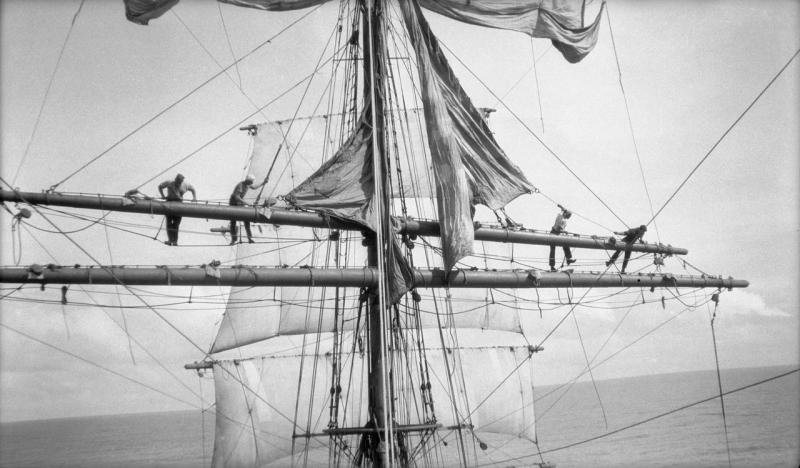 four sailors walk the foot-ropes while furling the main upper topsail