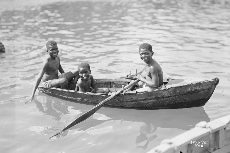 Three small diving boys in a locally constructed wooden rowing boat at Castries, St. Lucia, West Indies (P94762, © National Maritime Museum)