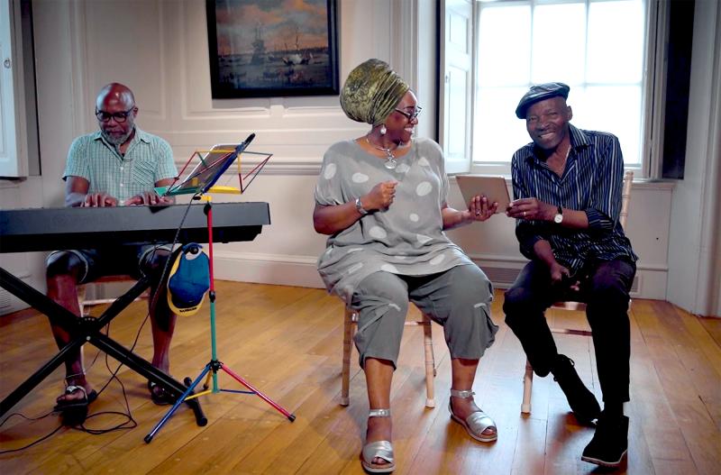 A group singing together, with a man playing a keyboard on the left and a woman and man sharing an iPad screen and singing on the right