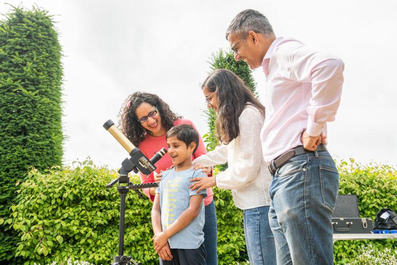 A young boy looks through a telescope at the Royal Observatory surrounded by his family