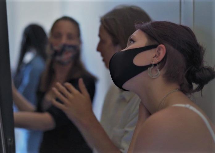 A woman wearing a mask looks up at an object to her left