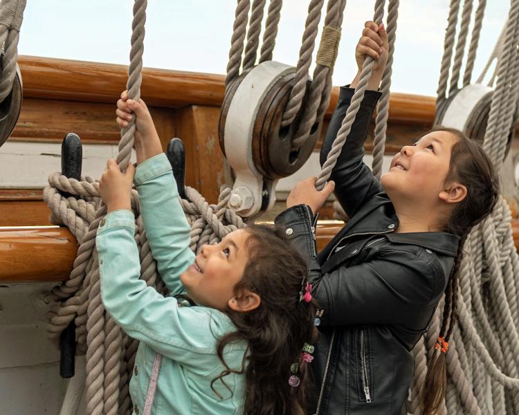 Two young children pull on ropes that act as part of the rigging for historic ship Cutty Sark