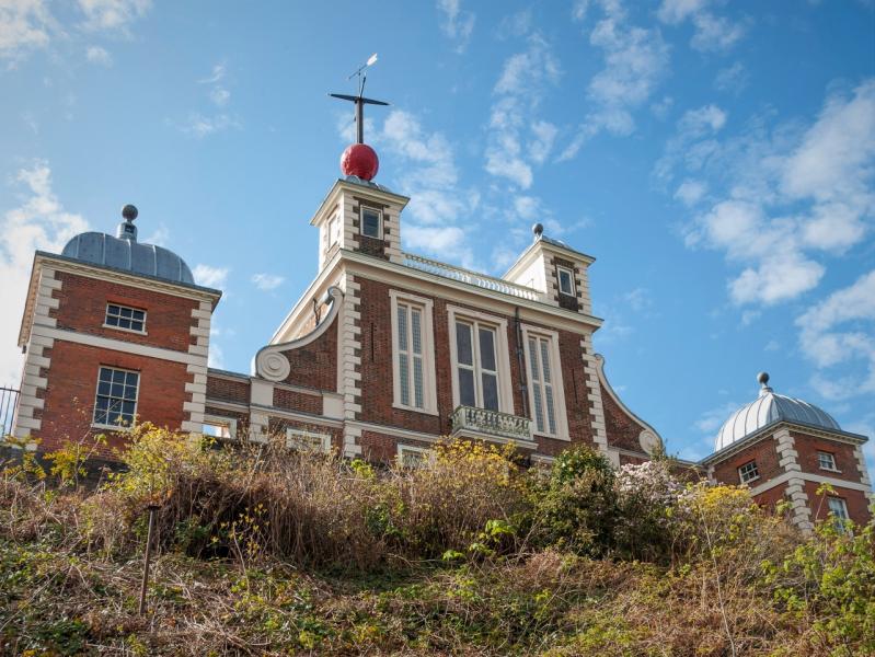 View of the Royal Observatory Greenwich from below. The brick facade of Flamsteed House and the red Time Ball on the roof are visible