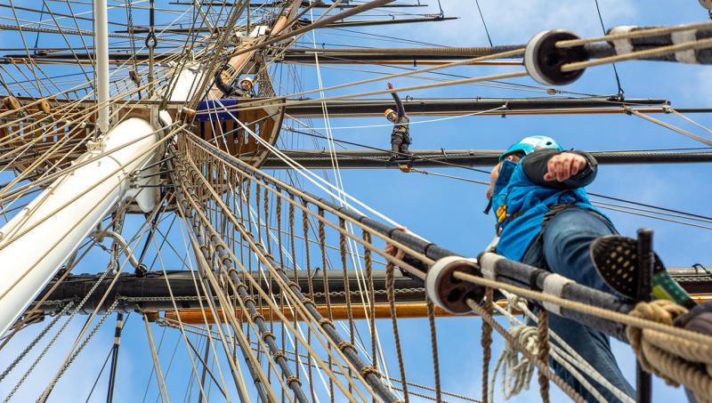 A man holding on to the ropes of Cutty Sark's rigging looks up at a platform positioned around the ship's main mast