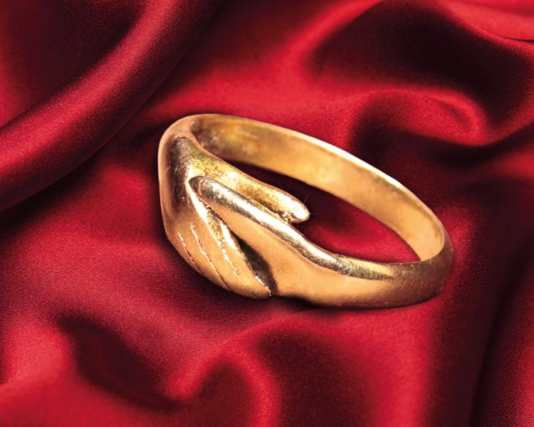 A gold ring designed to look like two clasped hands, set against a rich red background