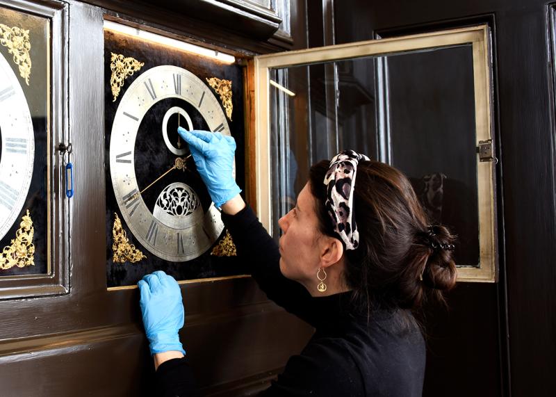 A woman wearing blue surgical gloves examines a historic clock during conservation work in the Royal Observatory's Octagon Room